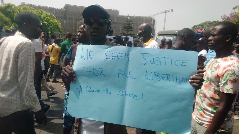 Un manifestant pose pour une photo sous la bannière « Save the State », photo de Mark N. Mengonfia, 7 juin 2019, Monrovia, Liberia, utilisée avec permission.
