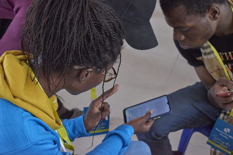 De jeunes Nigérians discutent du contenu d'une page Web ouverte sur un smartphone. Image de James Moore200 via Wikimedia Commons, 27 mars 2021, sous licence CC BY-SA 4.0.